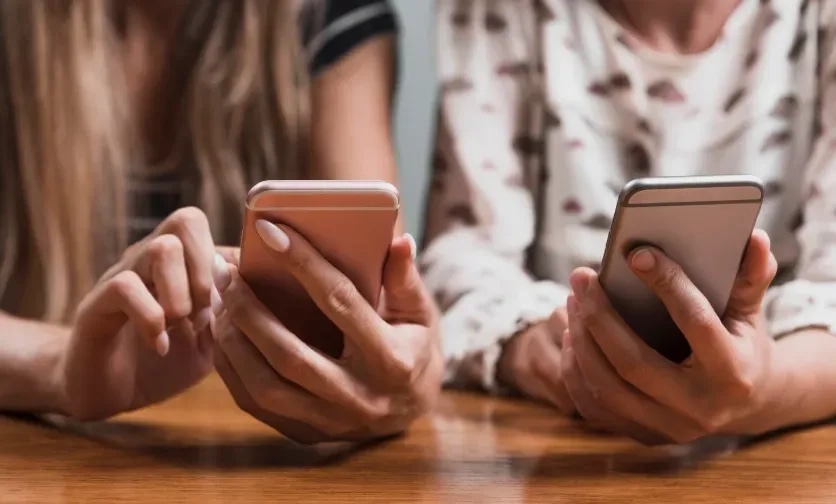Two friends sitting side by side, each holding a phone