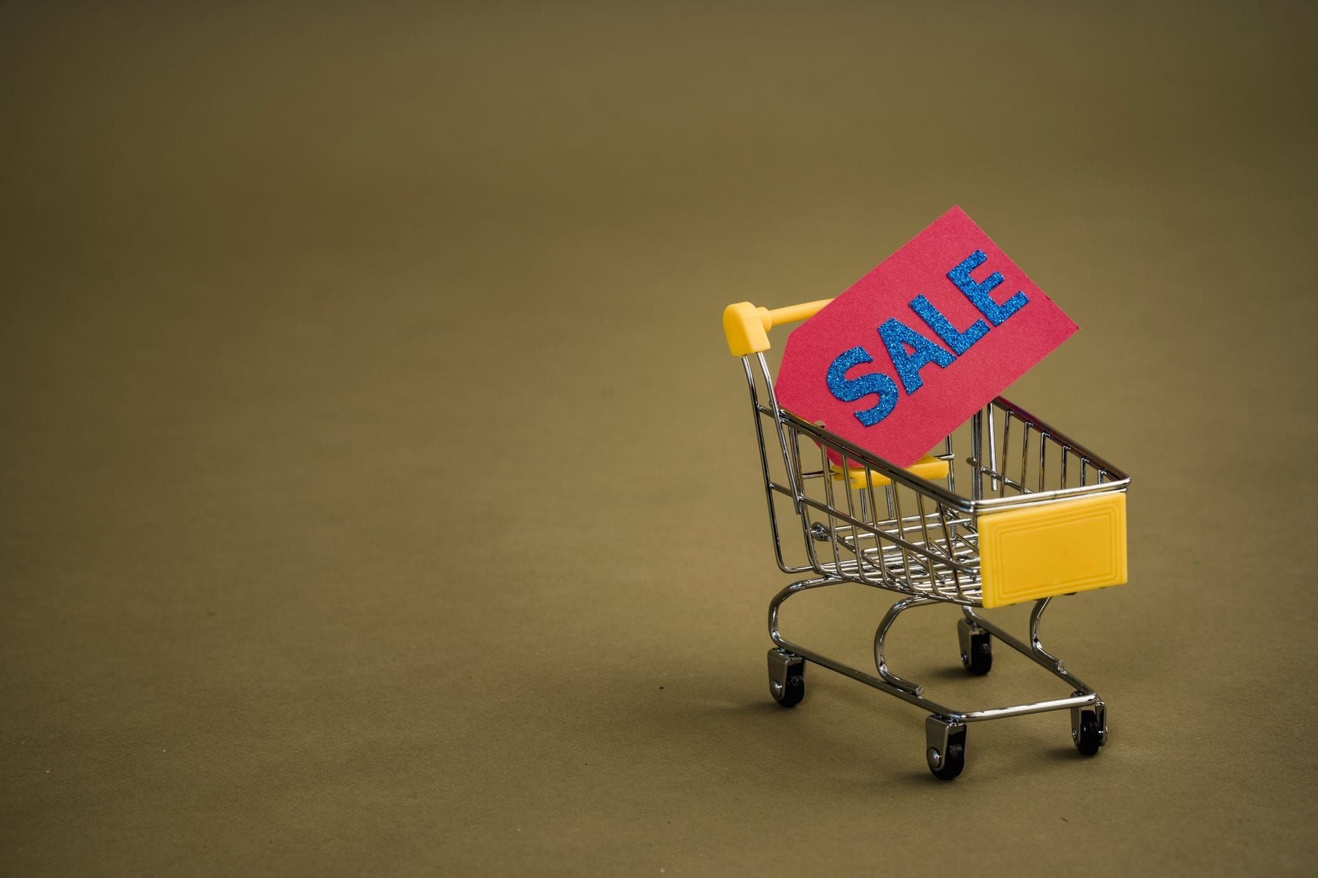 Miniature shopping cart holding a bright sale tag